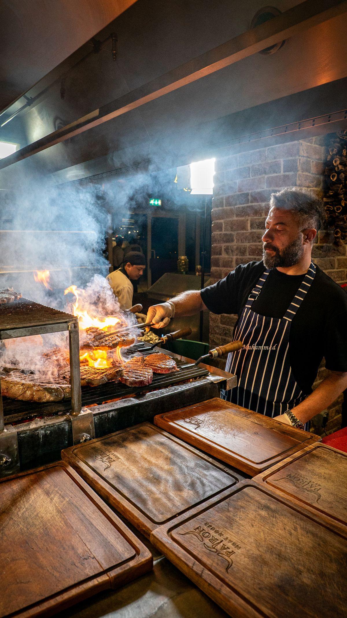 Chef in a striped apron grilling over open fire in the kitchen