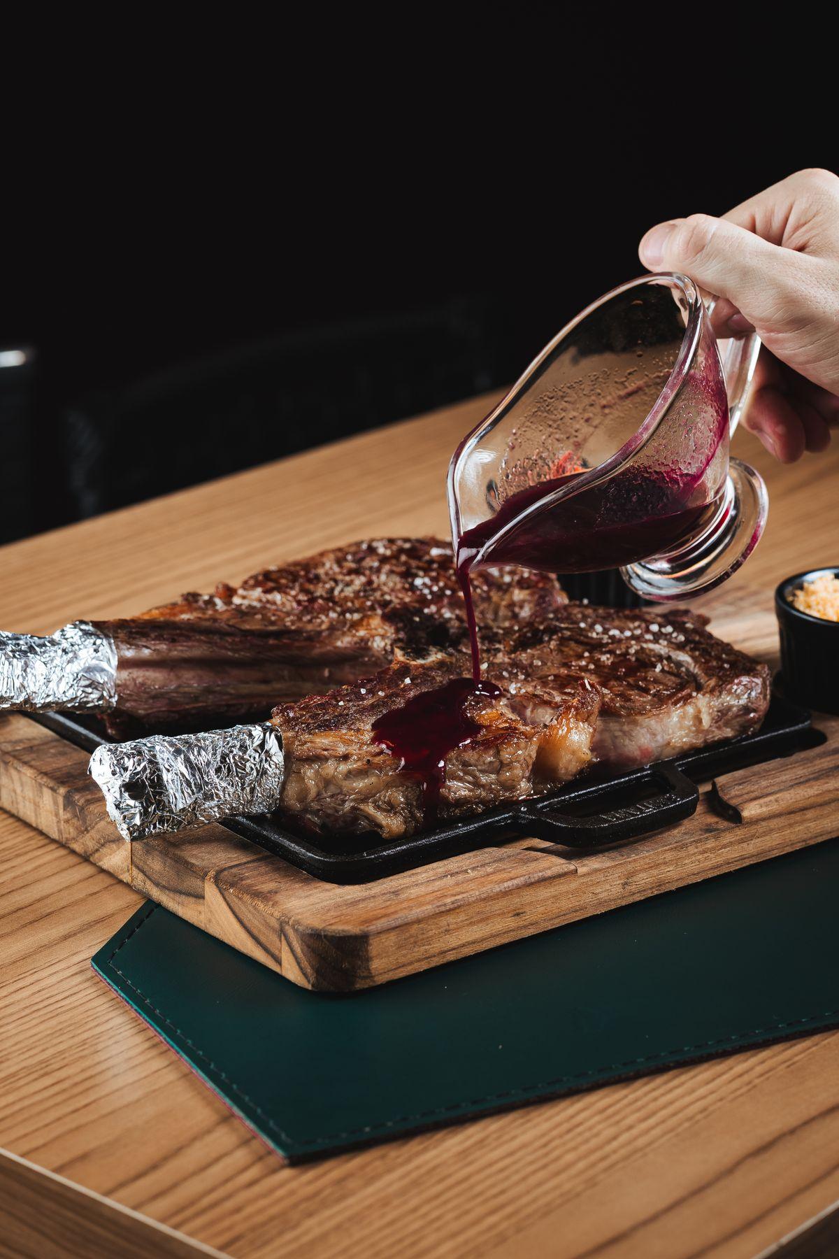 Steak on a cast-iron plate with red wine sauce being poured over it